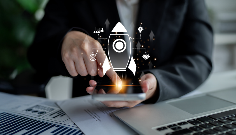 Hand einer Person in Businesskleidung, die auf ein Tablet mit schwebendem Symbol einer Rakete und Finanzgrafiken tippt